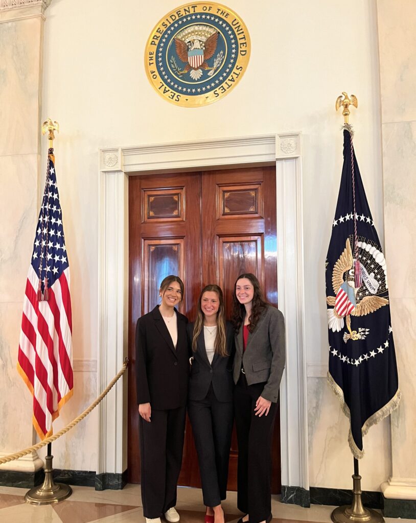 Natalie and 2 other students under the Seal of the President of the United States next to the American flag in the White House