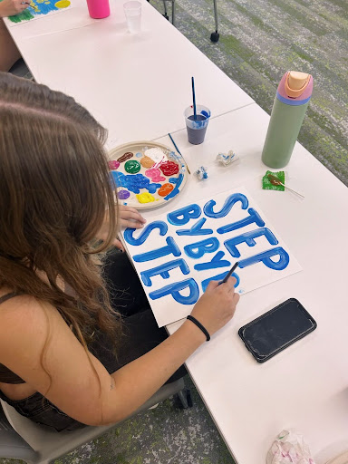 Members decorating posters that say "step by step" during a meeting