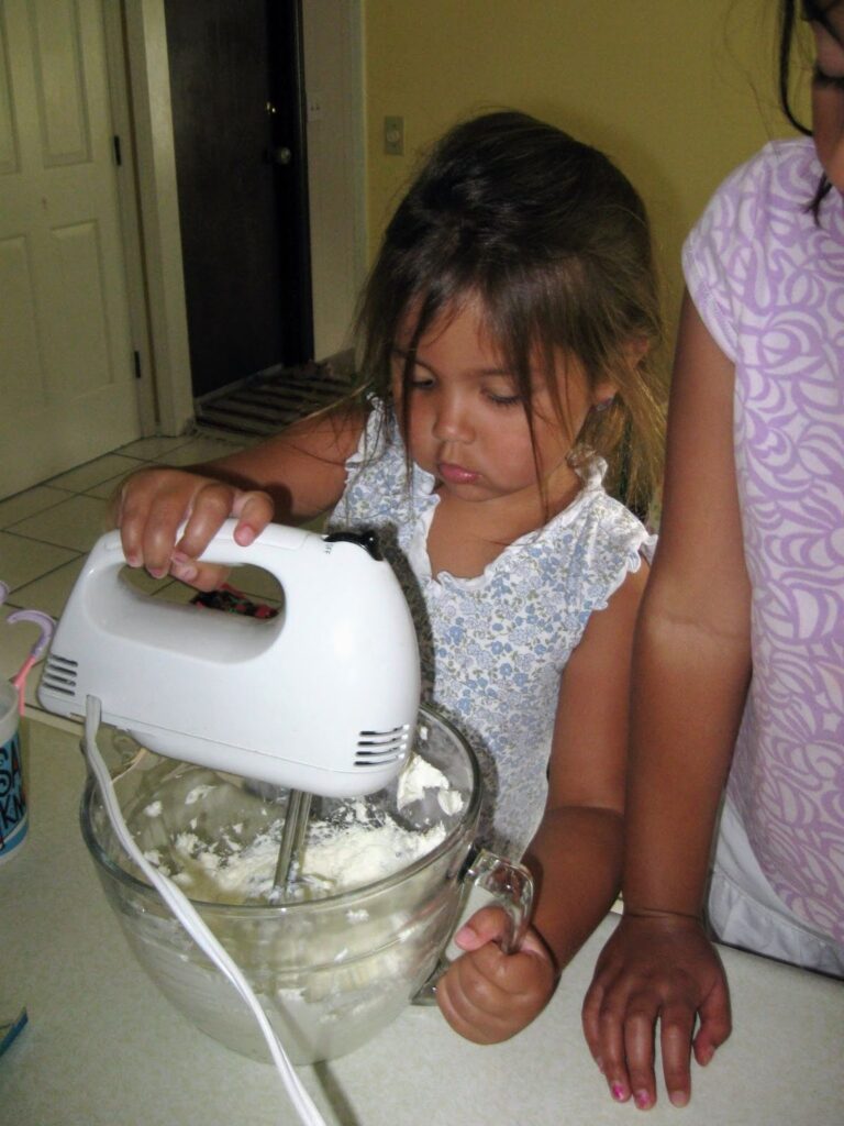 Child learning learning to bake with a hand mixer.