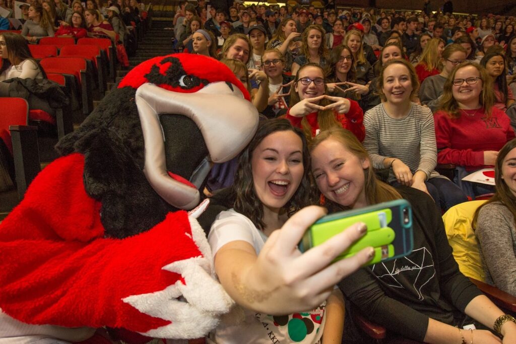 Miami University Swoop taking selfie with students at basketball game. 